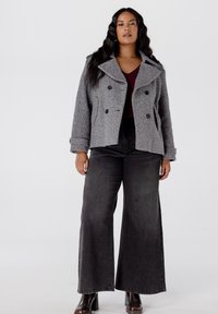 Grijze wolmix peacoat met een dubbelzijdig ontwerp en zwarte knopen, gecombineerd met brede, donkergrijze jeans en bruine hoge laarzen.