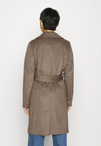 Bruine wollen jas met een kraag en riemdetails, met een getailleerde pasvorm en een rugsplit, gecombineerd met losse blauwe denim broeken.