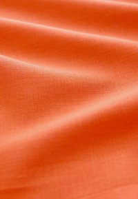 Texturierter oranger Stoff mit glatter Oberfläche, der einen dezenten Glanz und ein gewebtes Muster zeigt, drapiert, um Tiefe und Falten zu demonstrieren.