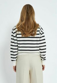 Prugasti pulover u crnoj i bijeloj boji, s ležernim krojem i rebrastim manžetama, u kombinaciji s bež hlačama koje imaju bočne džepove.