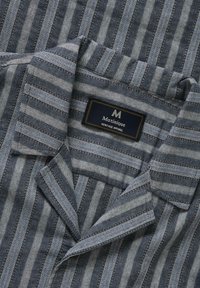 Chemise à col avec des rayures verticales dans des tons de gris et de bleu, avec une étiquette Matinique Heritage Apparel à l'intérieur du col.