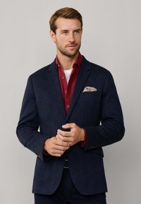 Granatowy blazer o fakturze z klapami typu notch, dwoma przednimi kieszeniami i brązową chusteczką w paisley, nałożony na burgundową koszulę.