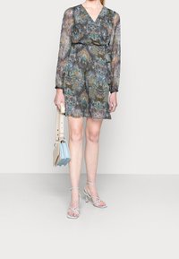 Průhledné šaty s dlouhým rukávem v barevném paisley vzoru s překládaným designem a páskem. V kombinaci se světle modrými sandály na podpatku a strukturovanou kabelkou.