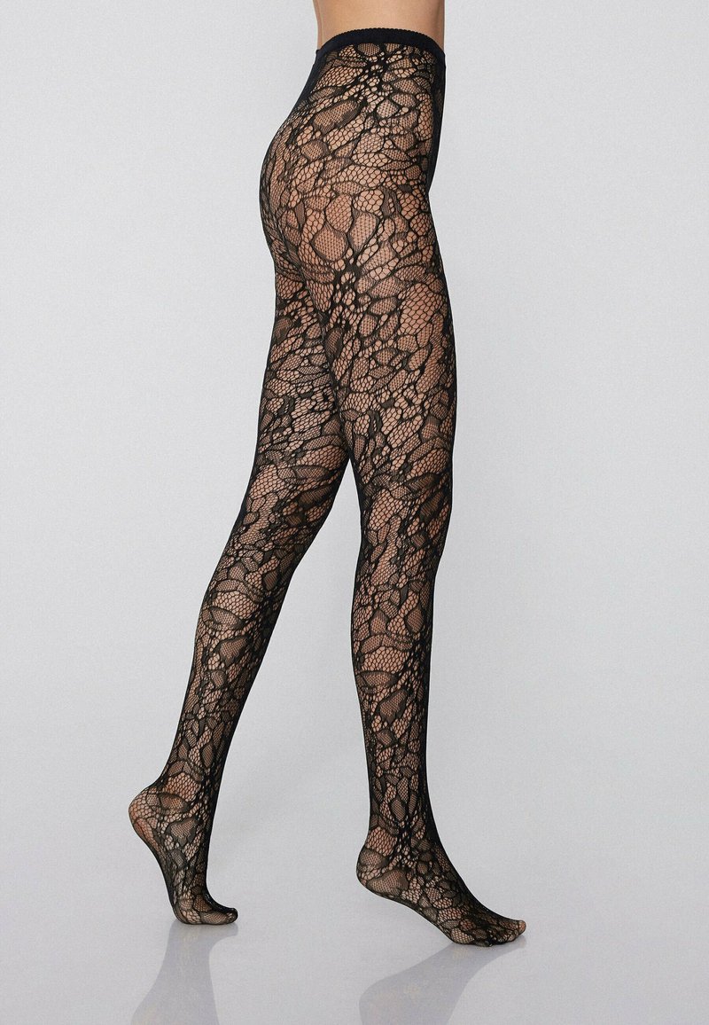 Collant in pizzo nero con un motivo intricati, caratterizzati da una lavorazione a rete e una vita liscia. Texture trasparente, punte dei piedi in vista.