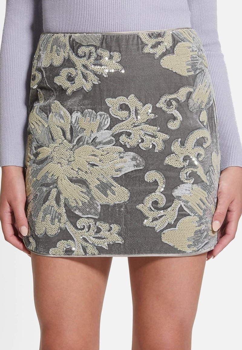 Jupe courte en velours gris avec une grande broderie florale crème en sequins, portée avec un haut côtelé lavande à manches longues.