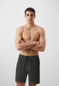 Fekete úszóshort, rugalmas derékkal és zsinórral, fehér varrással, egyenes fazonnal és egy kis logóval a bal lábon.