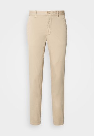 Beżowe bawełniane chinosy o prostym kroju, z zapięciem na guzik i przednimi kieszeniami. Gładka faktura bez widocznych wzorów czy akcentów.