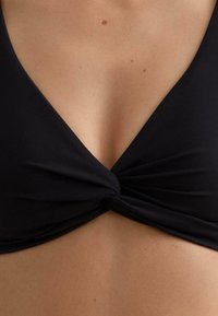 Čierny bikini top s hlbokým výstrihom do V a spleteným uzlom v strede. Hladká textúra a minimalistický dizajn bez ozdôb.