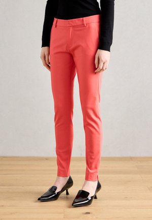 Korálové slim-fit kalhoty s hladkým povrchem, zdobené předními sklady a poutky na pásek, kombinované s černými lodičkami s špičatou špičkou.