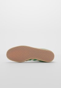 Sneaker con una parte superiore in maglia verde e bianca, caratterizzata da due strisce verdi. La suola in gomma ha una texture a nido d'ape di colore beige chiaro.