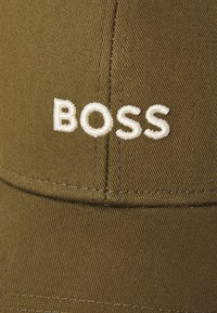 Maslinasto zelena pamučna kapa s izvezenim natpisom "BOSS" u bijelom koncu, strukturiranog dizajna i glatke teksture.