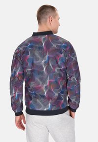 Multicolore patroon bomberjack met golvende ontwerpen, een zwarte kraag, elastische manchetten en een gestructureerde afwerking. Grijze sweatpants zichtbaar.