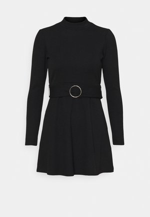 Robe noire en tricot à manches longues avec un col montant, une jupe évasée et une large ceinture ornée d'une grande boucle circulaire argentée à la taille.