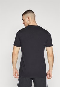 Sort kortærmet t-shirt lavet af bomuld, med rund halsudskæring og en afslappet pasform, vist fra ryggen uden synlige logoer.