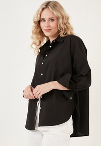 Black button-up shirt with a relaxed fit, featuring long sleeves and a rounded hem. Made from lightweight fabric with a smooth texture.