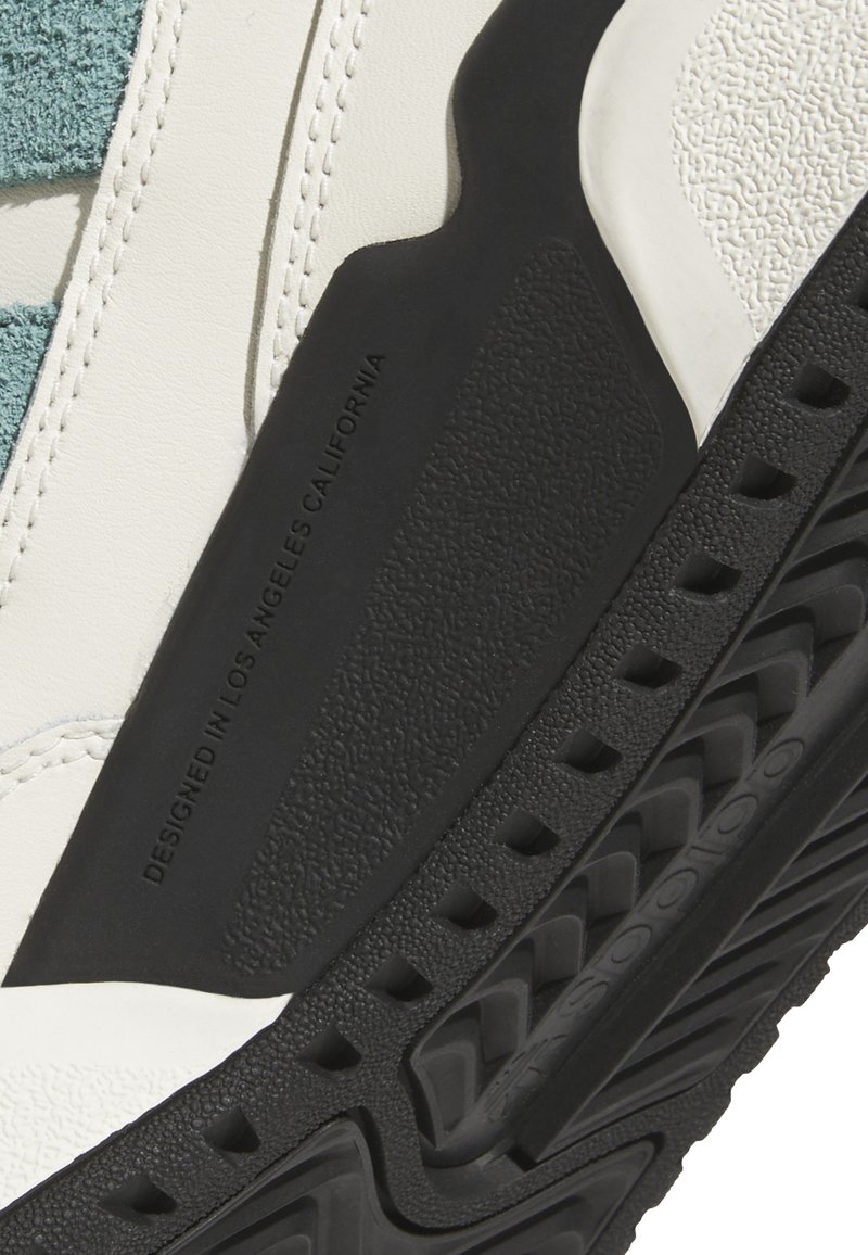Baskets avec une tige en cuir blanc, des accents en daim teal, une semelle en caoutchouc noir texturée et un détail gravé "CONÇU À LOS ANGELES CALIFORNIE".
