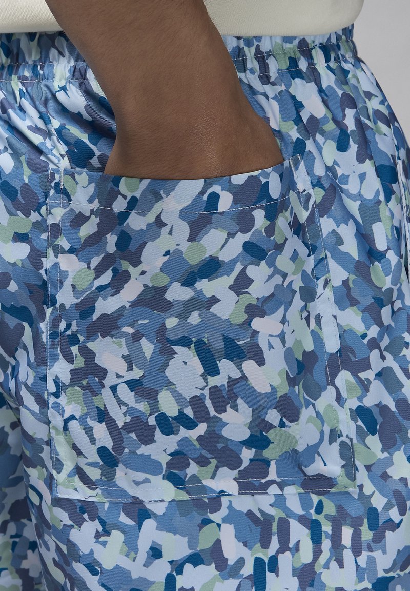 Shorts à motifs bleus avec une grande poche à rabat. Le matériau présente des formes abstraites dans des nuances de bleu, de vert et de blanc. Taille élastique.