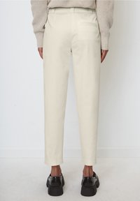 Helle beigefarbene maßgeschneiderte Hose mit geradem Bein und seitlichen Taschen, ausgestattet mit einer Gesäßtasche und getragen mit klobigen schwarzen Schuhen.