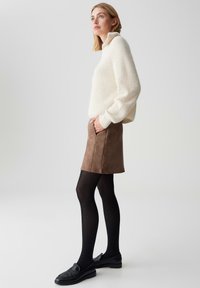 Weißer gerippter Pullover, brauner Wildleder-Minirock, schwarze Strumpfhosen und schwarze Slipper. Taschen auf dem Rock sichtbar; overall entspannte Passform.