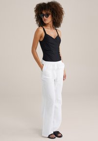 Must-valge ühes tükis ujumistrikoo, millel on südamekujuline krae; koos lahtiste valgete lina pükste ja mustade sandaalidega, mis on mugava lõikega.