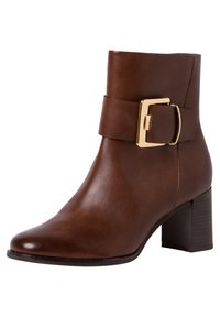 Bottine en cuir marron avec un bout carré, un large talon et une grande sangle avec une boucle en métal doré. Texture lisse.