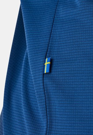 Niebieska tkanina o fakturowanym wzorze kratki z małą doszytą metką przedstawiającą żółto-niebieską flagę Szwecji.