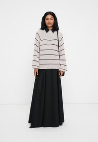 Beige gestreifter Pullover mit schwarzen horizontalen Linien, kombiniert mit einem langen schwarzen Rock. Der Pullover hat einen runden Ausschnitt und lockere Ärmel.