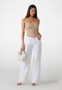 Body beige a costine con un nodo frontale, abbinato a pantaloni bianchi a gamba larga. Accessoriato con una piccola borsa bianca e sandali rosa.