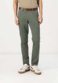Pantalons en coton verts avec une coupe droite, dotés de poches latérales et d'une ceinture en cuir marron, associés à des chaussures blanches avec des accents noirs.