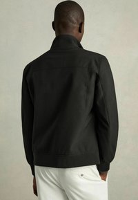 Zwarte jas met hoge kraag, ribbelboorden en zoom. Glad stofoppervlak en minimalistisch ontwerp, met een strakke achterkant.