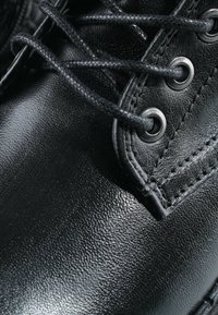 Gros plan sur une chaussure en cuir noir avec des coutures détaillées et des lacets noirs passés dans des œillets métalliques.