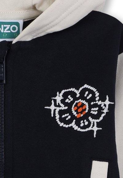 Giacca a cappuccio in felpa blu navy con accenti color crema, caratterizzata da un ricamo floreale bianco e arancione sulla parte anteriore e una chiusura con zip.