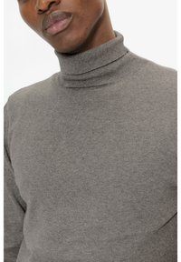 Pull col roulé gris avec une coupe ajustée, une texture lisse et douce, des poignets côtelés, mettant en valeur une finition sans couture autour du cou.