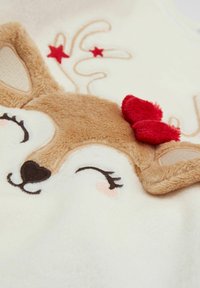 Cremefarbener Fleece-Stoff mit einem Rentiergesicht, braunem Fell, bestickten Augen und einer roten Schleife als Akzent an einem Geweih.