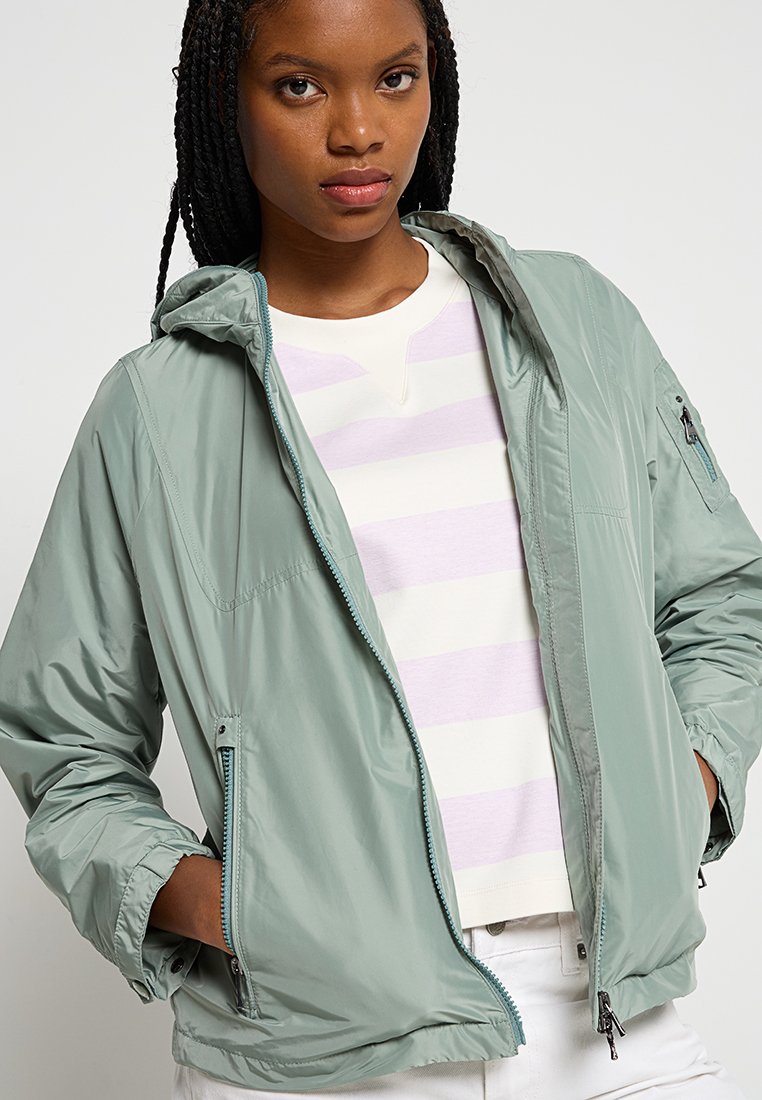 Hellgrüne, zip-feste Jacke mit Kapuze, aus glattem, leichtem Material; mit Seitentaschen und sichtbaren Nähten.