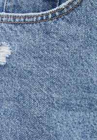 Denimtyg som visar en blekt blå färg med ett slitet område. Texturen är jämn med en lätt mjukhet, och sömmarna är synliga.