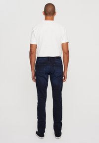 Tamno plavi traperice ravnog kroja, s stražnjim džepovima, nošene s običnom bijelom majicom i crnim tenisicama.