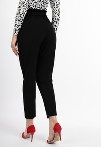 Zwarte hooggetailleerde broeken met een gathered taille en smalle pijpen, gecombineerd met rode hoge hakken. Glad textuur, minimale details.