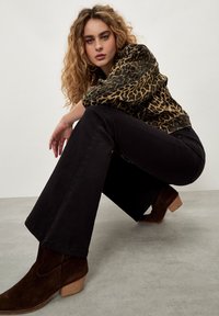 Veste en tissu léopard avec pantalon noir évasé et bottes chelsea en daim marron. Tissu texturé, design ajusté et pose décontractée.