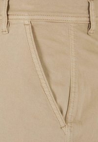 Beige Baumwollhosen verfügen über eine vordere Tasche mit verdeckter Naht und einer glatten Textur, die für Komfort und Tragekomfort konzipiert sind.