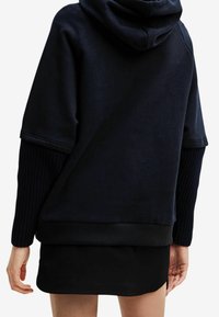 Sudadera negra extragrande con mangas acanaladas, tejido suave y capucha con cordón. Presenta un ajuste relajado y una longitud recortada.