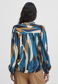 Mehrfarbige Bluse mit einem wellenförmigen Muster in Blaugrün, Braun, Creme und Marineblau, mit einem gerafften Kragen und langen Puffärmeln.
