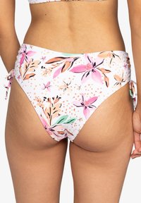 Bas de bikini blanc avec un motif floral en rose, orange et vert. Il dispose de liens sur les côtés et d'un tissu texturé. Logo Roxy visible.