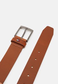 Cintura in pelle marrone con una fibbia in metallo argentato di forma rettangolare, con un accento del logo. Texture liscia, estremità affusolata e multiple forature per la regolazione.