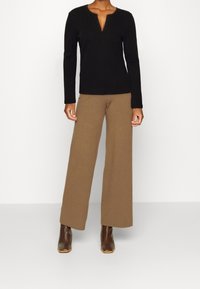 Schwarzes Langarmoberteil mit Rundhalsausschnitt und Ausschnittdetails, kombiniert mit braunen, weiten Hosen und braunen Stiefeletten. Schlichtes Design und strukturiertes Material.