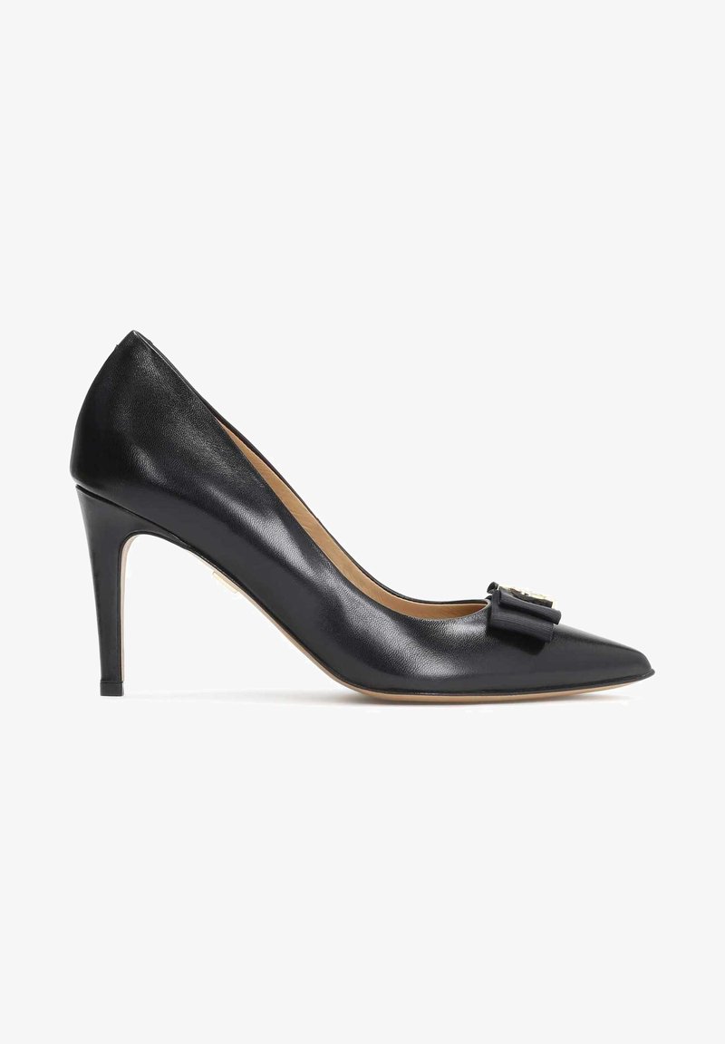 Zapato de tacón alto de cuero negro con punta afilada, que presenta un detalle decorativo de lazo y un delgado tacón de aguja. Textura suave.