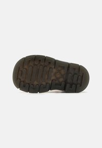 Suela de zapato de goma negra con un patrón texturizado. Presenta surcos y crestas para mayor tracción, con una sección ligeramente transparente cerca del borde.