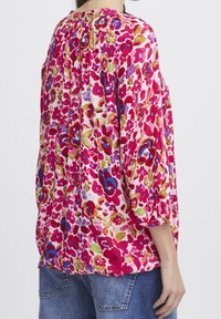 Blommig blus med ett livfullt mönster i rosa, rött och grönt, med lös passform och rynkad halsringning. Långa ärmar och lättviktig tyg.