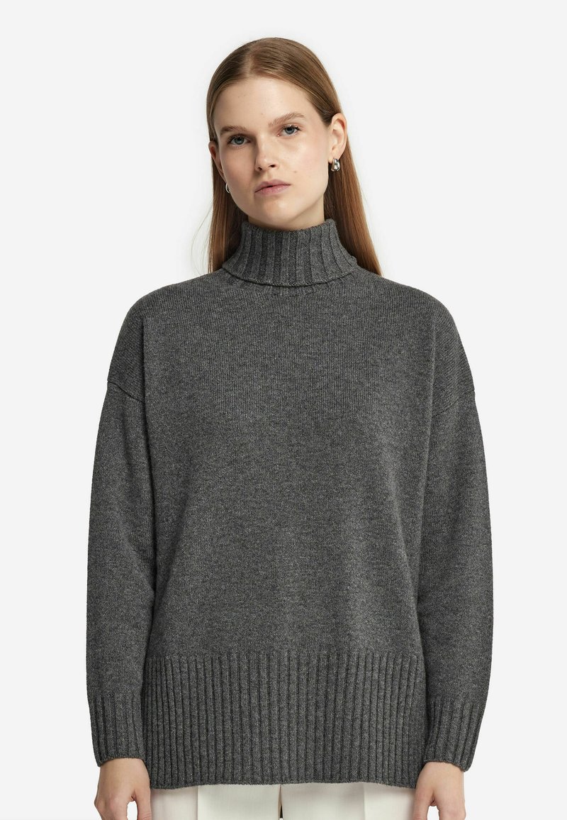 Pull en tricot gris à col roulé avec un ourlet et des poignets côtelés. Coupe oversize et texture douce, descendant jusqu'aux hanches pour une silhouette décontractée.