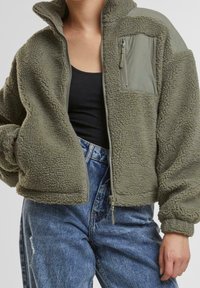 Olivengrüne Fleecejacke mit hohem Kragen, Reißverschluss vorne und einer Brusttasche; besteht aus einem weichen, strukturierten Stoff und hat gerippte Bündchen.